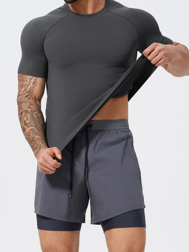 Male model stretch-testing dark grey seamless vented raglan short sleeve athletic tee, paired with 2-in-1 layered quick-dry training shorts, stretch moisture-wick performance knit for gym & casual streetwear.