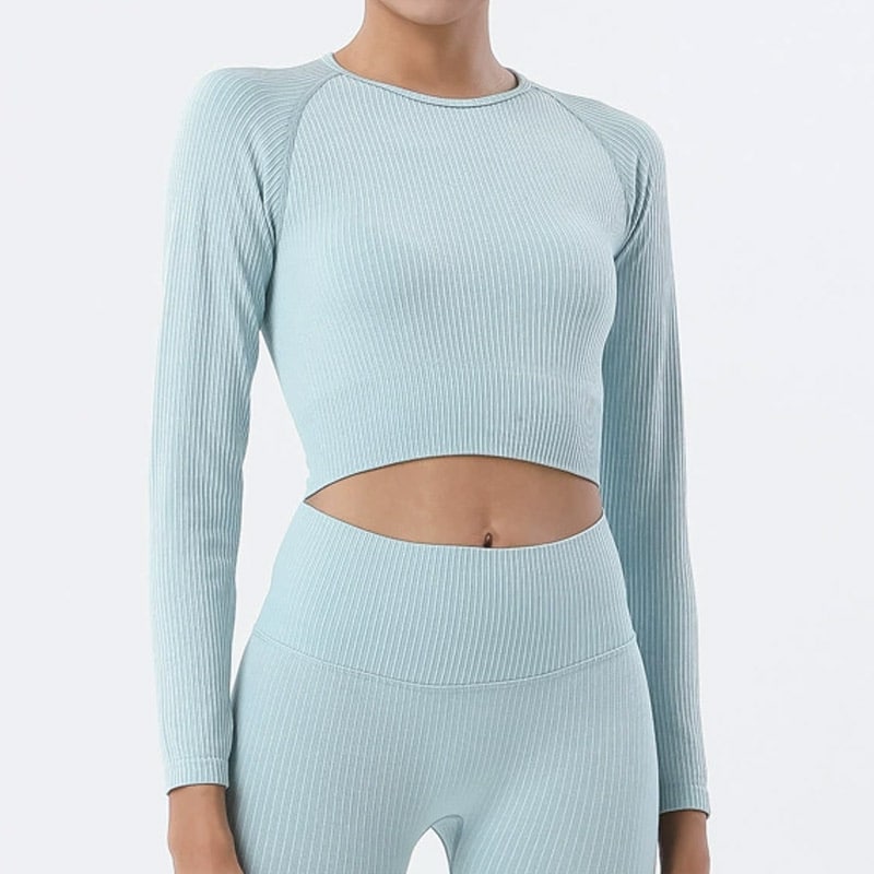 Studio front shot of womenโs light blue ribbed seamless crop top set, crew neck raglan long sleeve cropped athletic top, full vertical rib stretch knit, matched high waist ribbed leggings, soft moisture-wicking nylon spandex fabric, slim fitted silhouette for yoga, gym training and casual athleisure, wholesale ribbed seamless crop top OEM supplier.