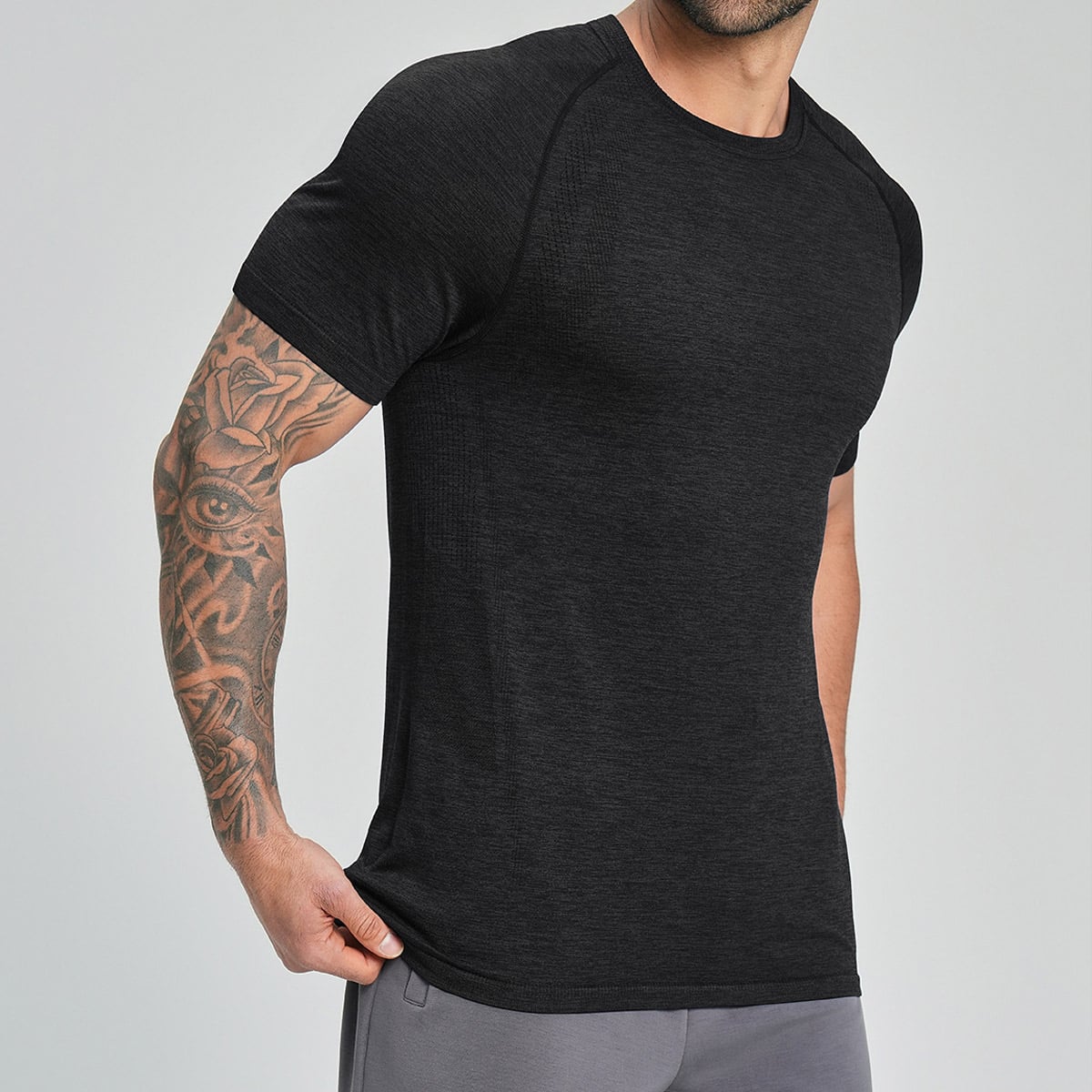Side studio shot of menโs black heather seamless t-shirt, classic crew neck raglan short sleeve, slim compression fit, lightweight heather performance knit fabric, seamless vented body construction, moisture-wicking anti-odor material for gym, crossfit, running and casual daily wear, direct black mens seamless t-shirt manufacturers wholesale supply.
