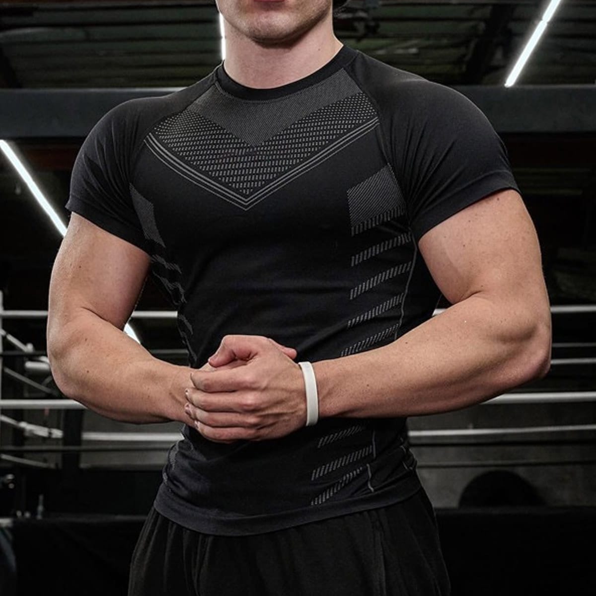 Gym studio shot of menโs black seamless performance short sleeve athletic tee, crew neck raglan cut, geometric jacquard mesh ventilation panels on chest & sides, compression fit stretch nylon spandex knit, moisture-wick quick-dry breathable fabric for weightlifting, boxing, cross-training, OEM performance seamless activewear wholesale manufacturer.
