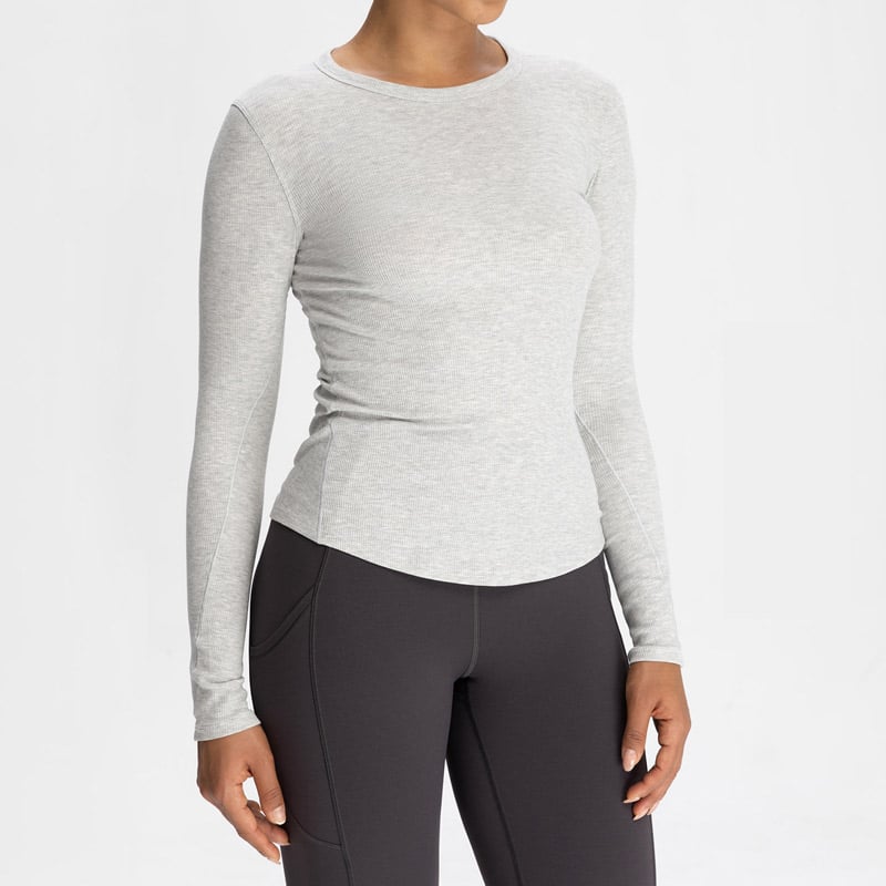 Unbranded light heather grey seamless long sleeve top blank, tag-free interior, stretch ribbed knit, plain smooth surface compatible with custom jacquard, screen print and embroidery logo branding, matched seamless legging blanks available for full set customization.