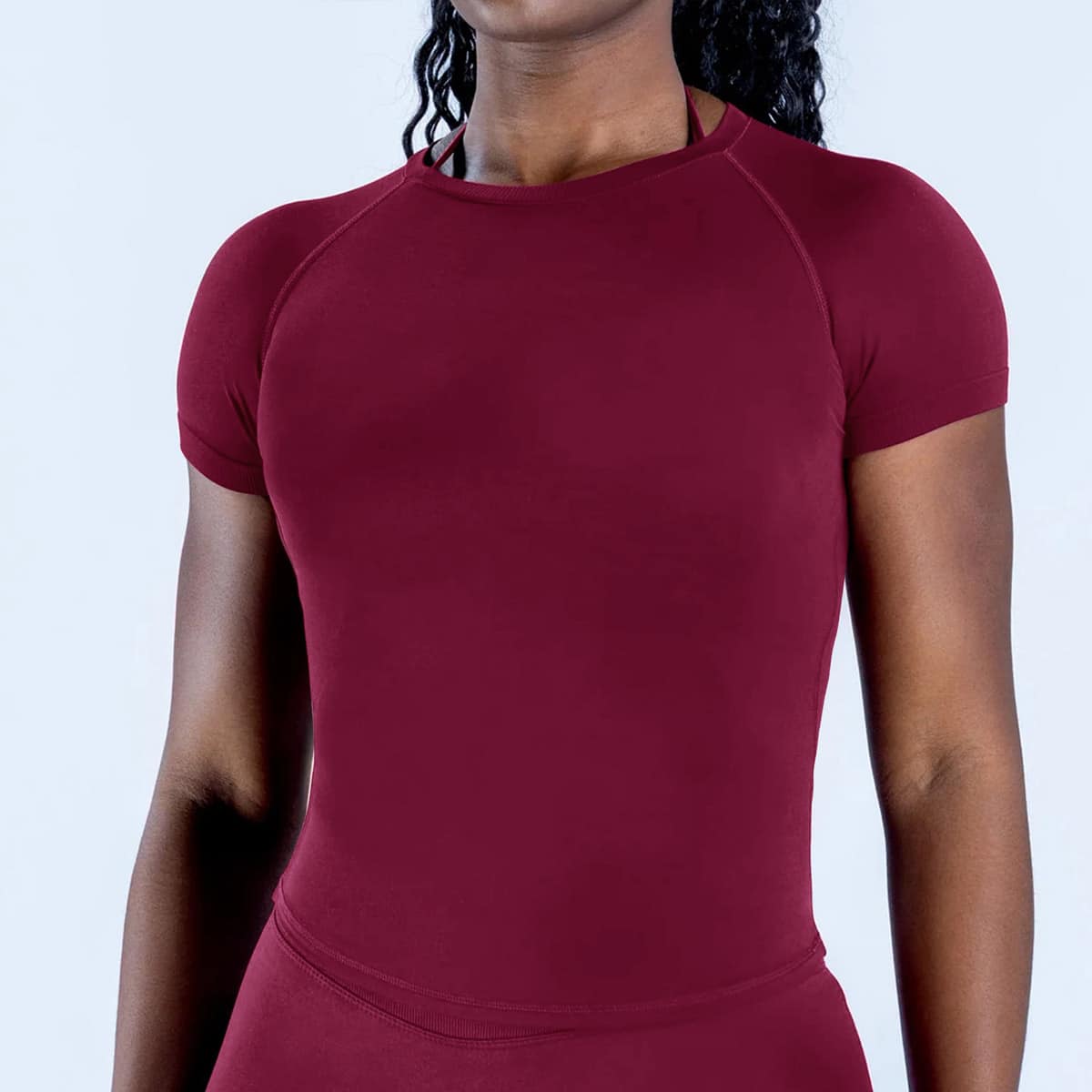 Front studio detail shot of womenโs burgundy custom seamless t-shirt, round neck raglan short sleeve, fitted compression silhouette, flatlock shoulder and side seams, smooth stretch performance knit fabric, breathable moisture-wicking fit for gym, yoga, running and everyday active layering, custom seamless t-shirts design OEM supplier.