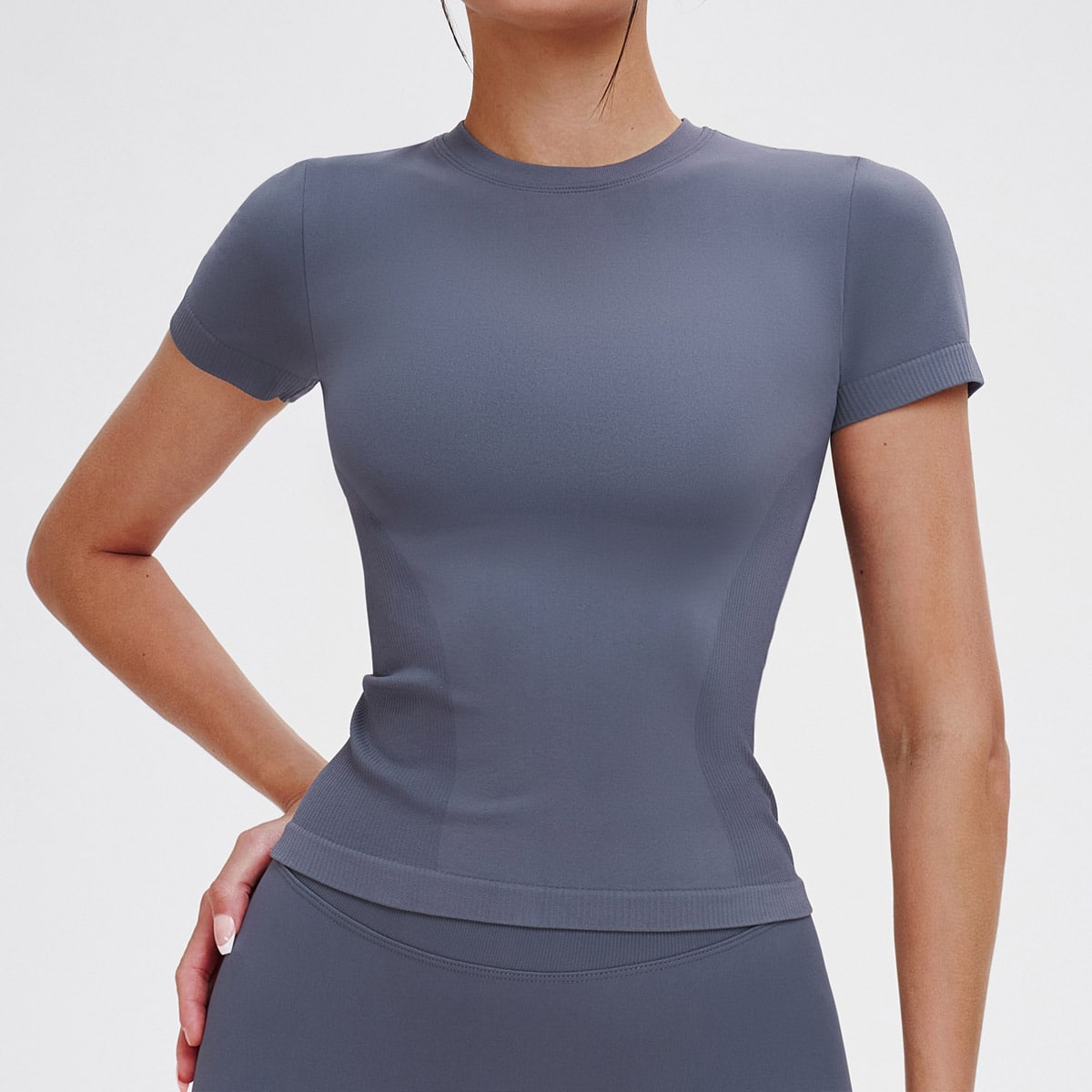 Front studio close-up of womenโs dusty grey seamfree t-shirt, crew neck raglan short sleeve, waist rib contour shaping panels, smooth naked-feel seamless stretch knit, tailored slim fit, moisture-wicking soft fabric for yoga, gym, daily casual wear, direct womens seamfree t-shirt manufacturers bulk wholesale supply.