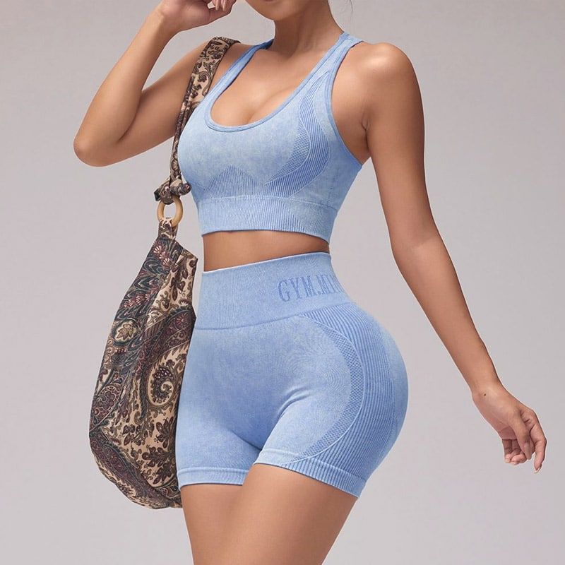 Front side studio shot of womenโs vintage wash light blue color block seamless yoga set, racerback medium-support sports bra with segmented textured color block panels, matching high rib waist biker shorts with curved rib contour zones, embossed waist logo detail, stretch nylon spandex knit, squat-proof moisture-wick fabric for yoga, gym and running, professional color block yoga sets OEM manufacturer.